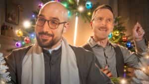 progressive Robot two men smiling in front of a decorated Christmas tree with colorful ornaments and lights