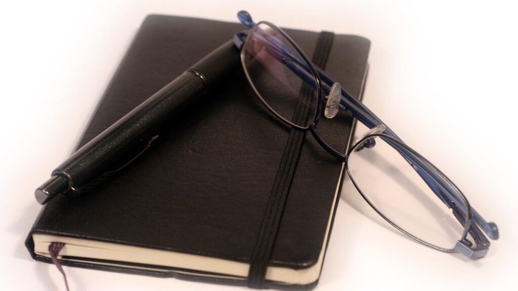 Diary, glasses, and pen used for meeting scheduling workflow planning