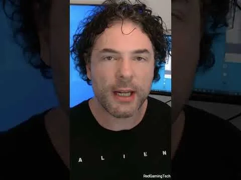 progressive Robot speaking to camera in front of a blue computer screen, wearing a black Alien T-shirt with text near bottom right