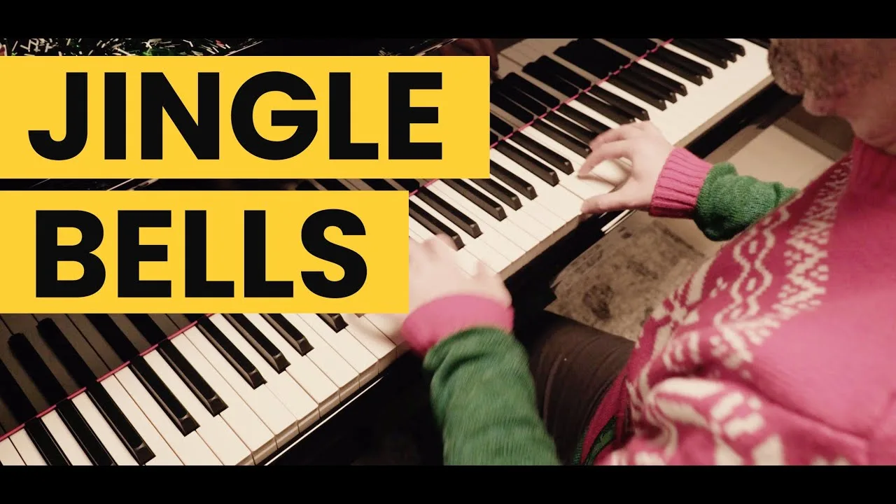 Progressive Robot, close-up of hands playing a piano with large yellow text reading “JINGLE BELLS”