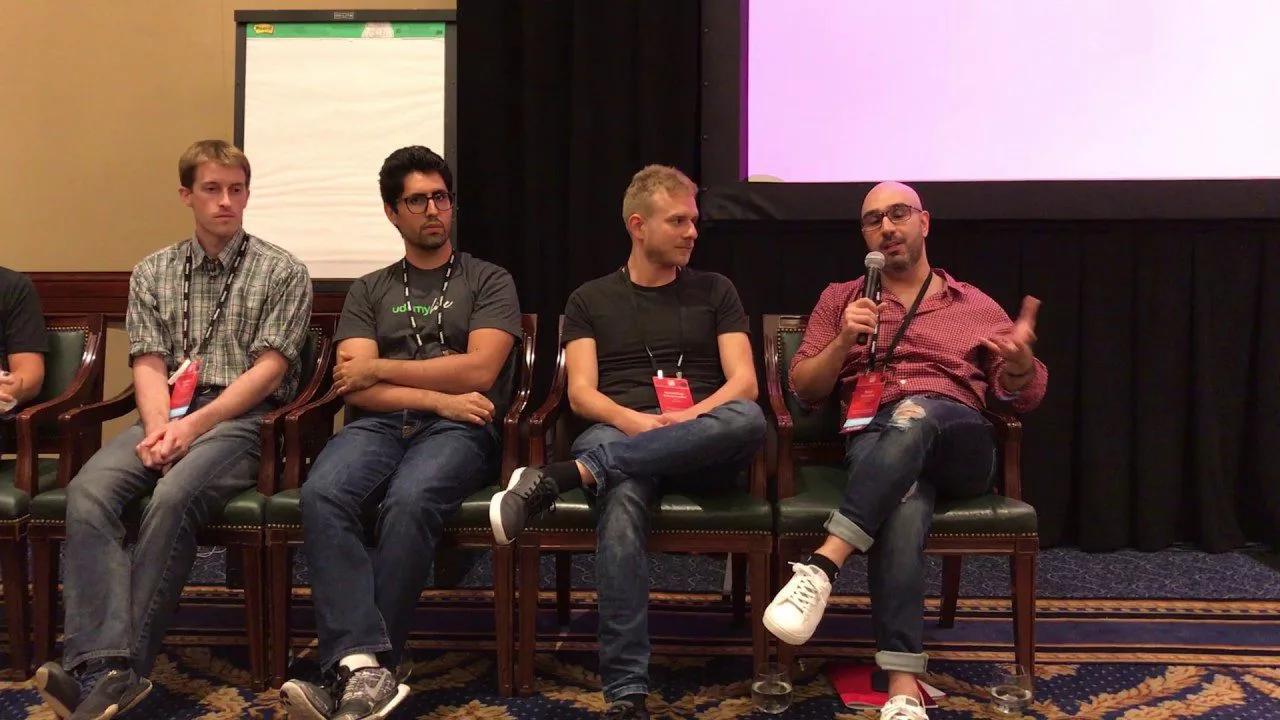 progressive Robot panelists seated on stage, one speaking into a microphone during a conference discussion