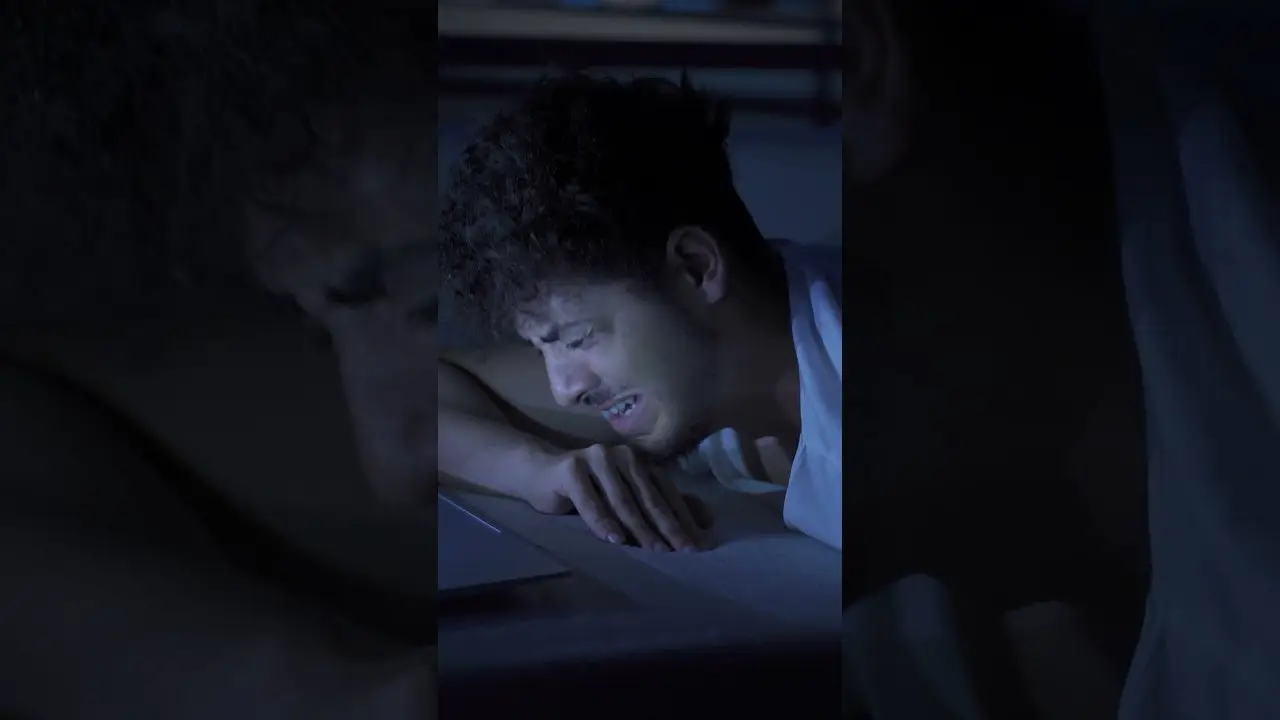 progressive Robot, man lying on a desk in dim blue light, face tense as if in pain or exhausted
