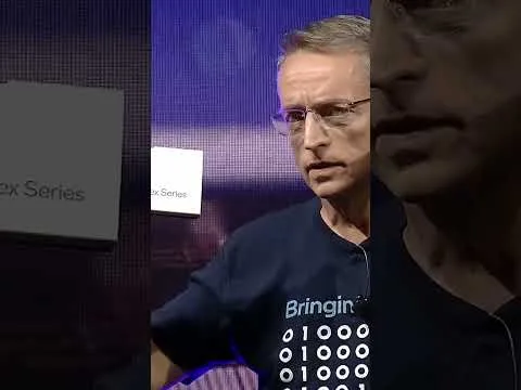 progressive Robot speaking on stage, wearing glasses and a dark T-shirt with binary digits on it