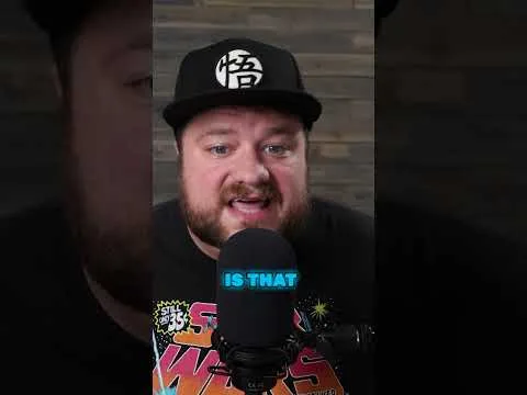 progressive Robot man speaking into a microphone, wearing a black cap with a white symbol and a graphic T-shirt against a wood wall