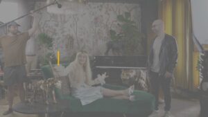 Progressive Robot Company film crew recording a woman on a green chaise in a decorated living room with tiger statues and piano