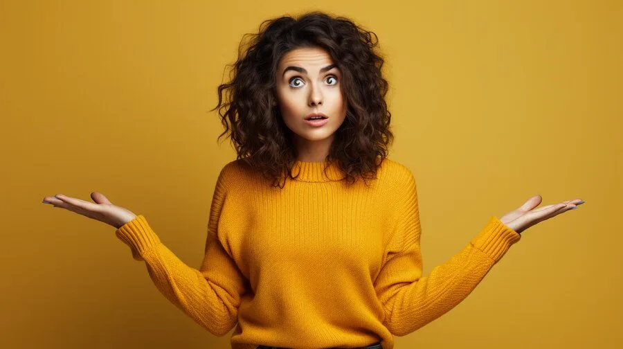 Progressive Robot: surprised woman in a mustard sweater with arms raised and palms up against a yellow background